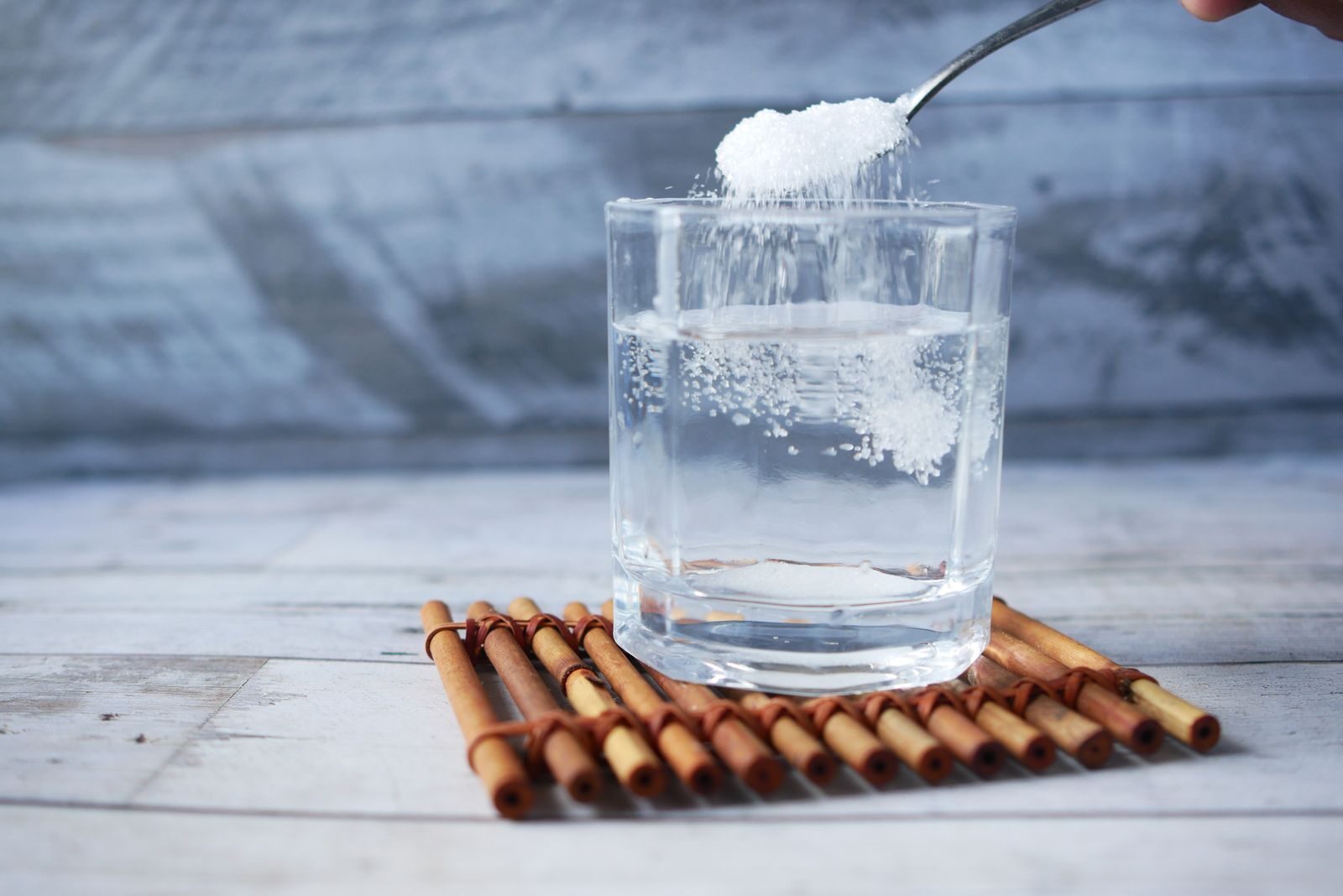 Photo by Towfiqu barbhuiya A spoonful of sugar being added to a glass of water on a wooden mat.