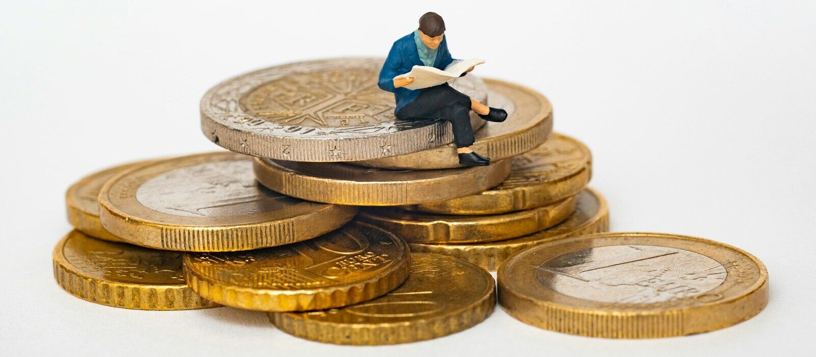 Miniature person sitting on stack of coins reading newspaper